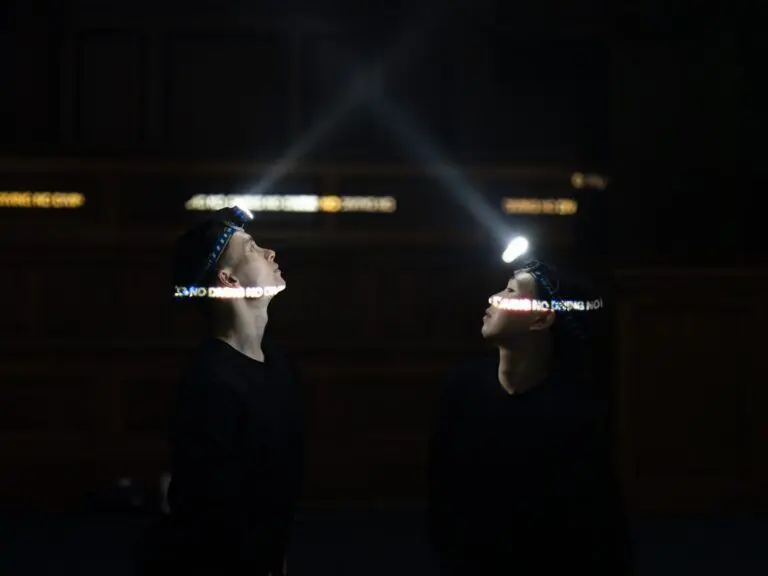 Two performers standing face-to-face wearing headlamps.