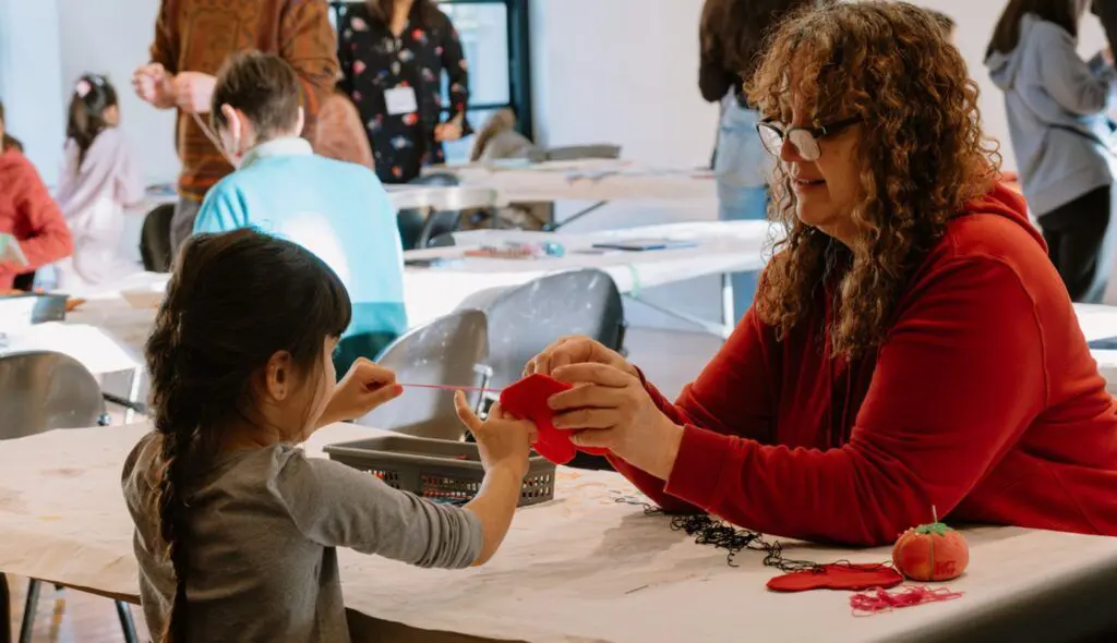 A woman and child engaged in an art-making activity together. The two are both holding a piece of felt while the child sews.