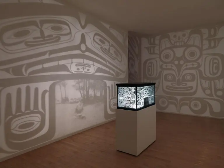 Installation by Marianne Nicolson with an object on a plinth in the centre of a room. The object looks like a bentwood box, and it shines light out on to the walls around it.