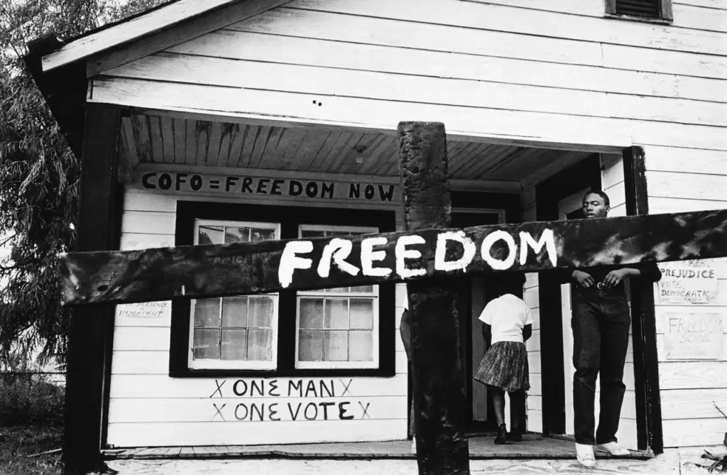 Black-and-white photograph with a house and a detail of a cross that reads "Freedom"