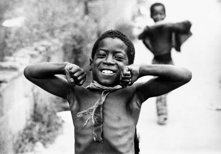 Black-and-white photograph of a Black boy in a Superman pose