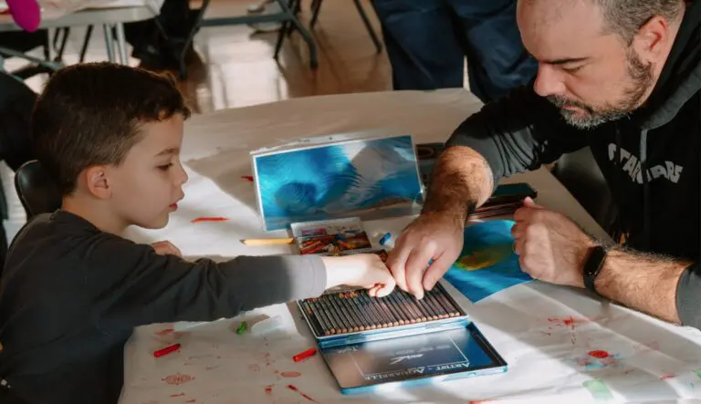 A father and son sit at a table and draw together.