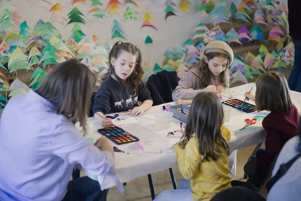 A group of one adult woman and four girls sit at a table painting.