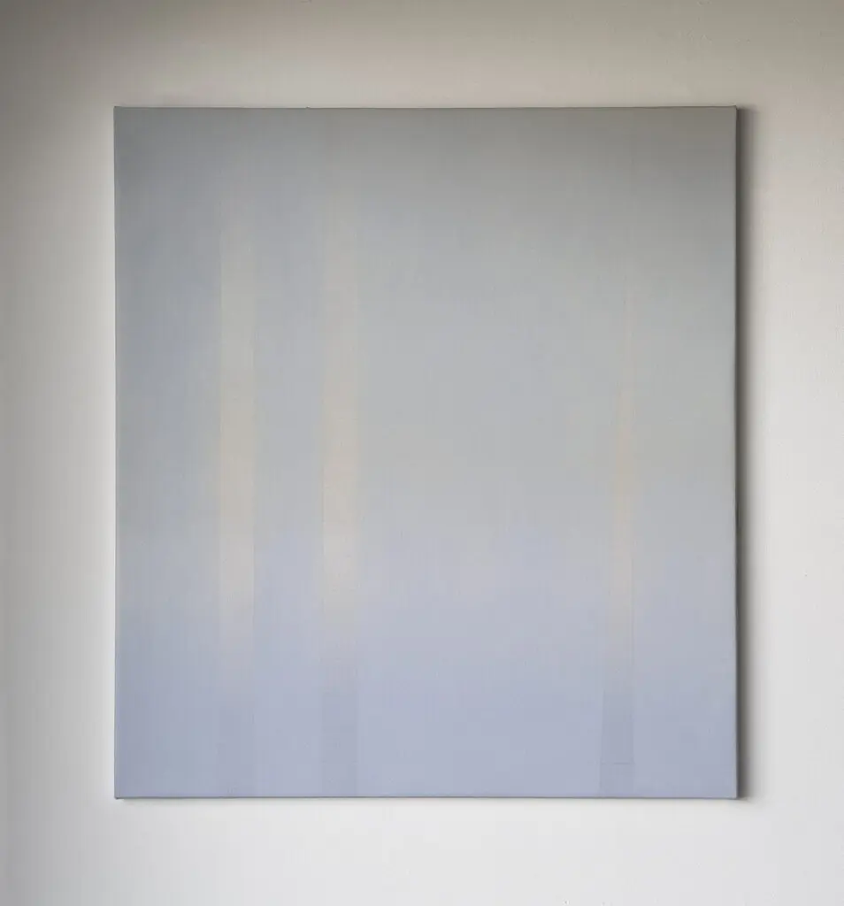 An image of a rectangular canvas on a white wall. The canvas is painted in a soft bluey purple colour, reminiscent of the sky.