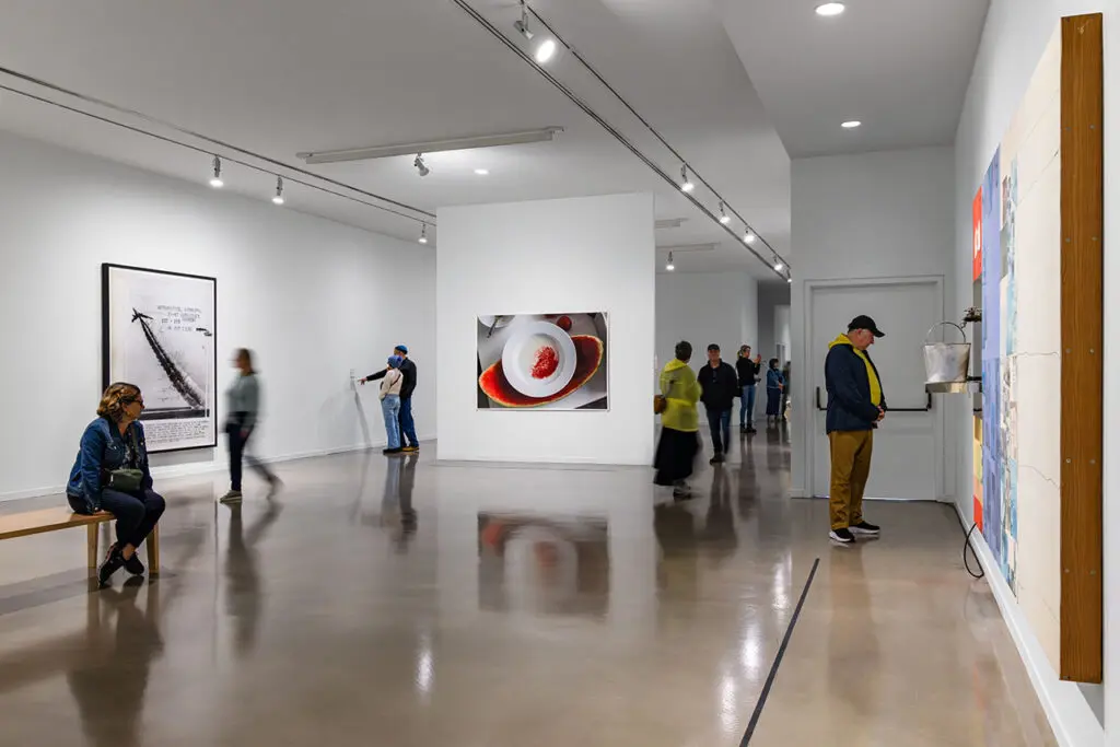 Visitors stand and sit looking at artworks in the exhibition Postcards from the Heart.