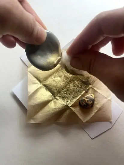 A photograph of two hands placing gold leaf as part of the Kintsugi process.