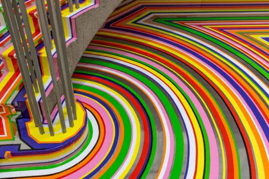 A detailed photograph of Jim Lambie's artwork on the Gallery Rotunda's floor. The shot is looking at a detail of the floor covered in brightly coloured strips of vinyl in purple, pink, green, red, orange and yellow.