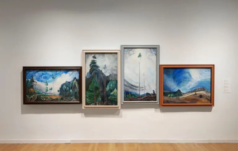 An installation photograph of 4 paintings by Emily Carr hung on the wall so that their horizon lines flow from one to the next.