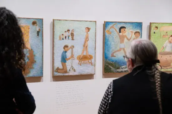 A photograph of a woman with grey hair in a braid from behind looking at paintings by Otani Workshop.