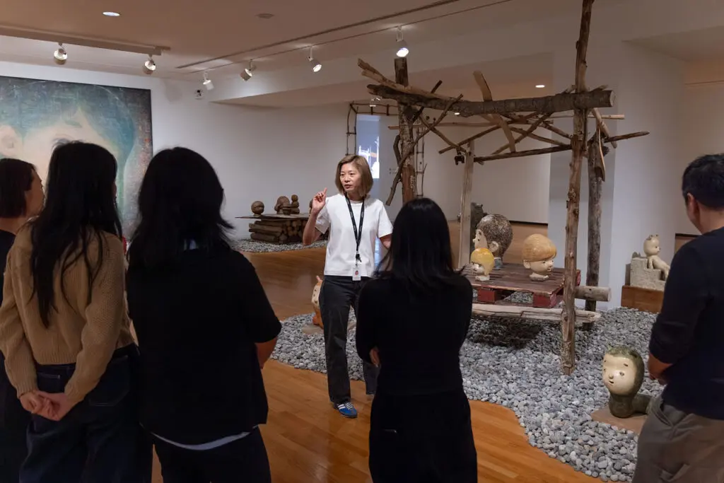 A photograph of a Gallery Tour at the Gallery in the exhibition "Otani Workshop: Monsters in My Head." We see the backs of 4 people looking at a female tour guide who is discussing Otani Workshop's work.