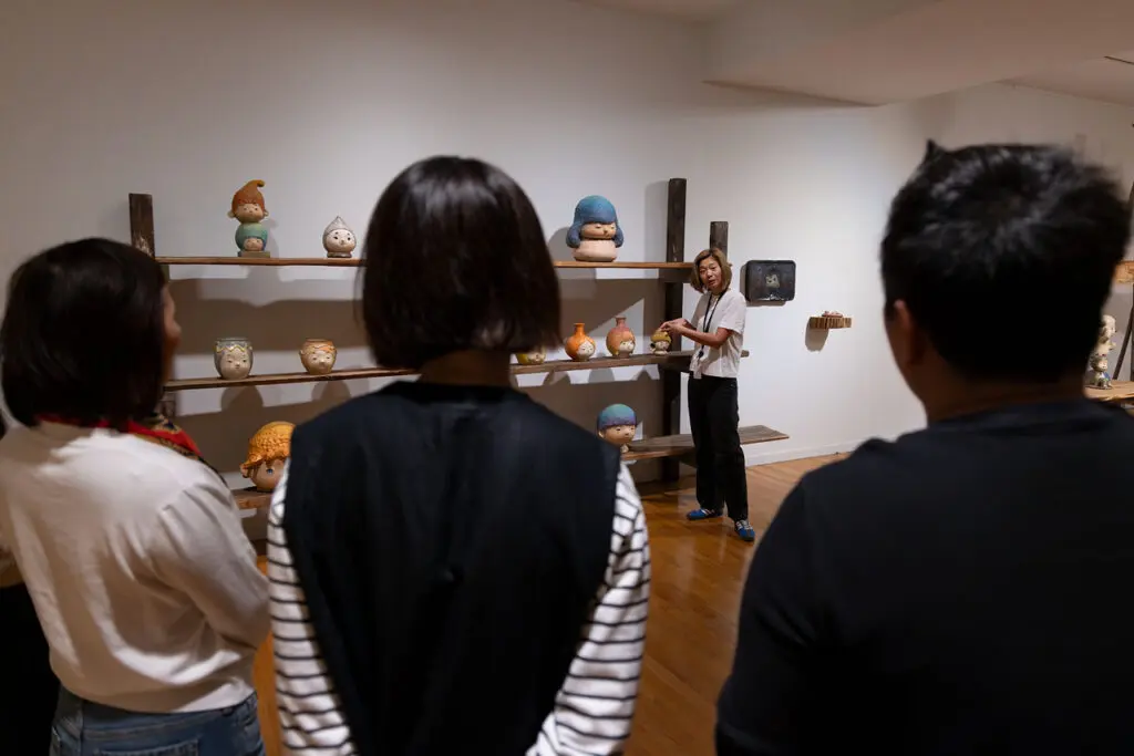 A photograph of a Gallery Tour at the Gallery in the exhibition "Otani Workshop: Monsters in My Head." We see the backs of 4 people looking at a female tour guide who is discussing Otani Workshop's work.