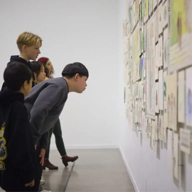 A group of students seen from the side looking at artwork on the wall.