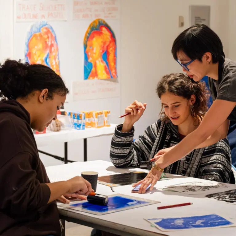 Square photograph of two teens sitting at a table completing a drawing exercise with artist Janet Wang.