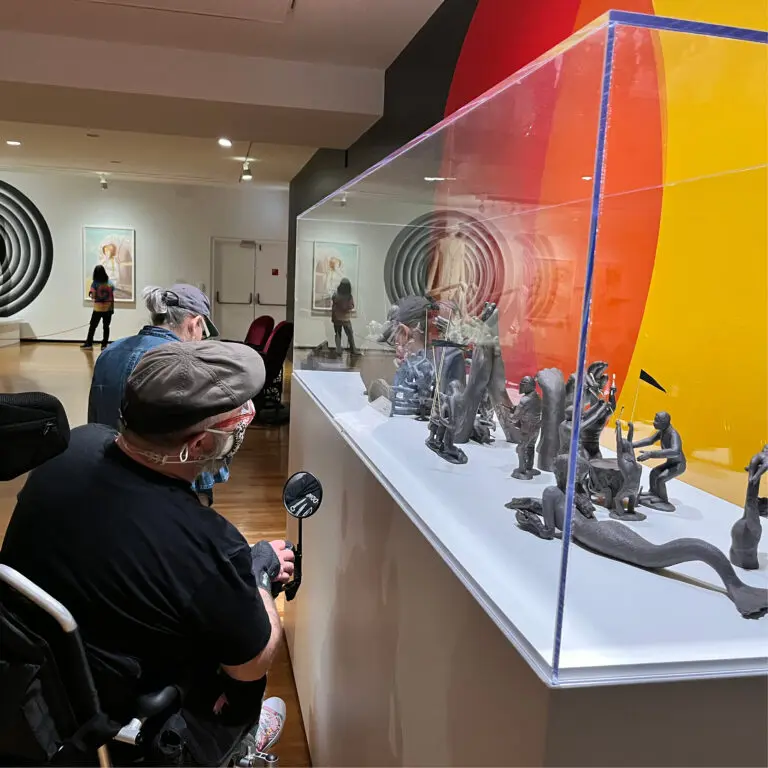 A square photograph of a man in a wheelchair looking at a plinth of sculptures.