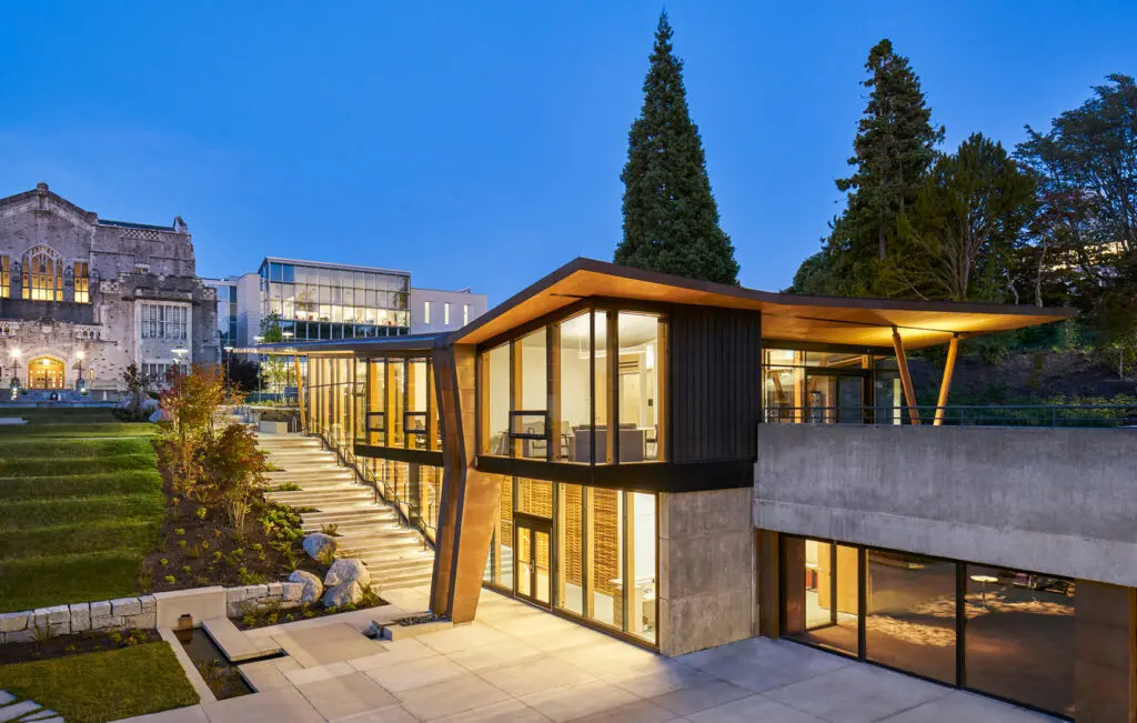 Photograph of a building low in the ground with large glass windows through which light emanates at dusk