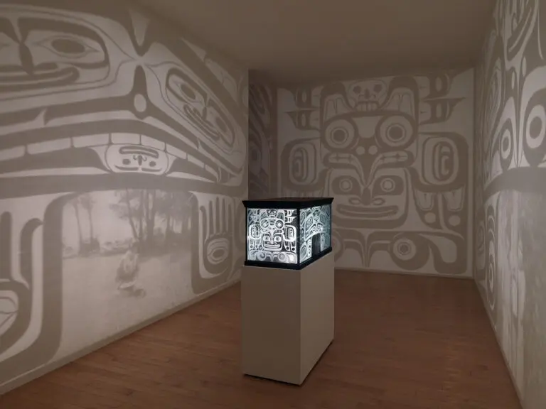 Installation by Marianne Nicolson with an object on a plinth in the centre of a room. The object looks like a bentwood box, and it shines light out on to the walls around it.