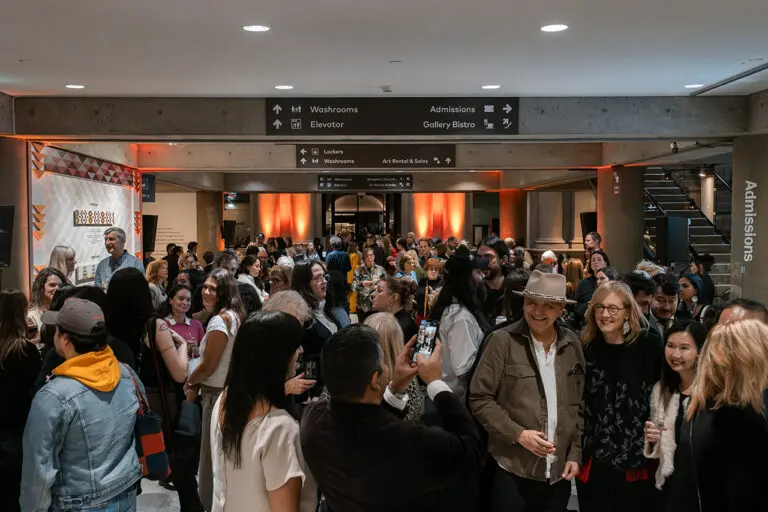 A photograph of the Gallery Lobby filled with people of all ages and backgrounds celebrating an exhibition opening.