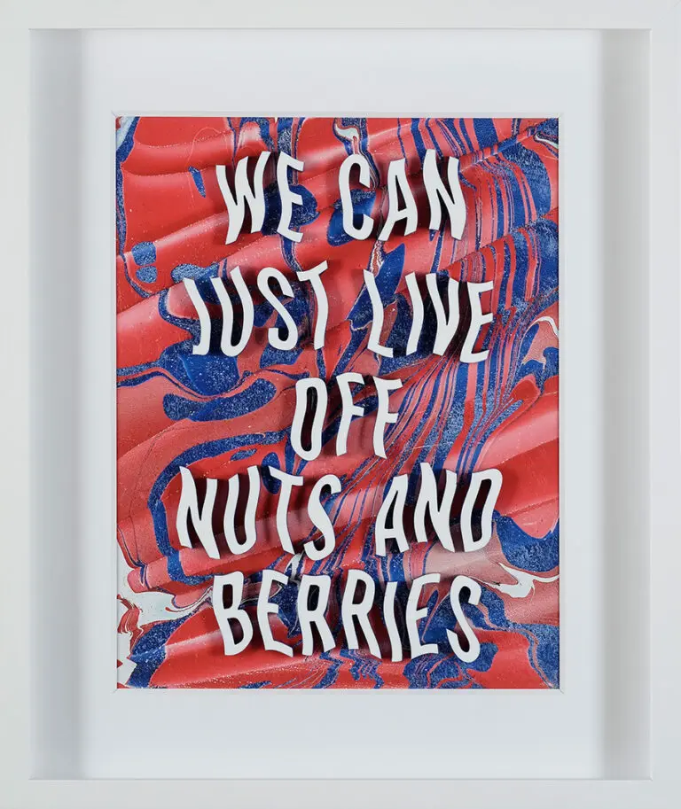 A photograph on an artwork in a white frame. The art is made up of text with red, pink and blue hues in the background. The text reads "We can just live off nuts and berries."
