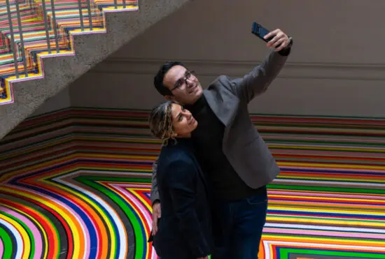 A couple stands in the Rotunda and take a selfie together. The Rotunda is covered in band of colour.