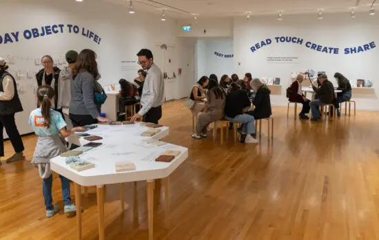 A photograph of visitors of all ages and background in the Vancouver Art Gallery exploring an interactive exhibition space where the can touch ceramic examples and read books and do activities.