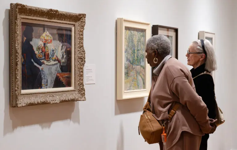 Two middle aged women look at paintings by Emily Carr on the Gallery wall
