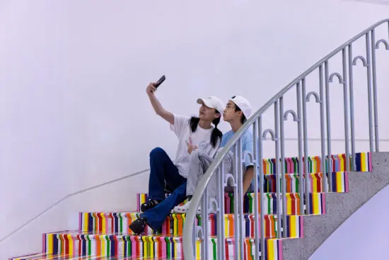 A mother and son sit on the colourful, striped stairs of the Gallery's Rotunda and take a selfie.