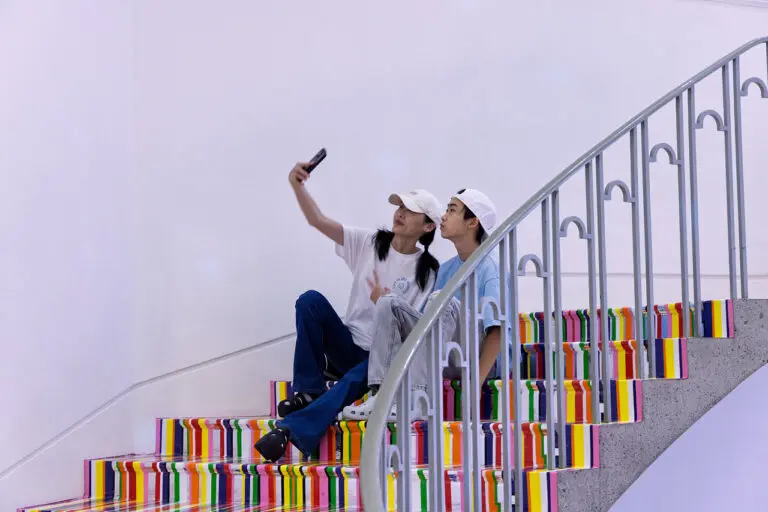 A mother and son sit on the colourful, striped stairs of the Gallery's Rotunda and take a selfie.