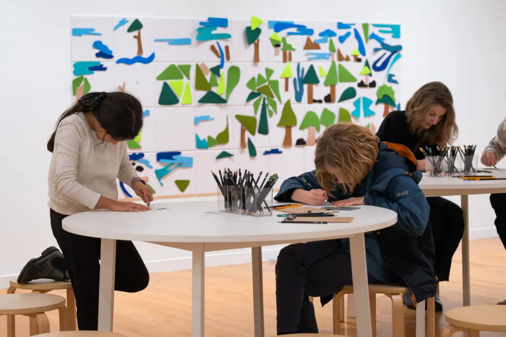 A boy and a girl sit around a table in the Gallery in the interactive space of That Green Ideal: Emily Carr and the Idea of Nature.