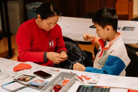 A photograph of a mother and son sitting at a table in The Making Place activity space. They are pulling a piece of yarn between them.