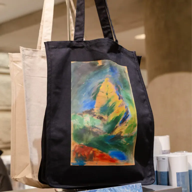 A photograph of a black canvas tote bag in the Gallery Store featuring a painting of a tree by Emily Carr