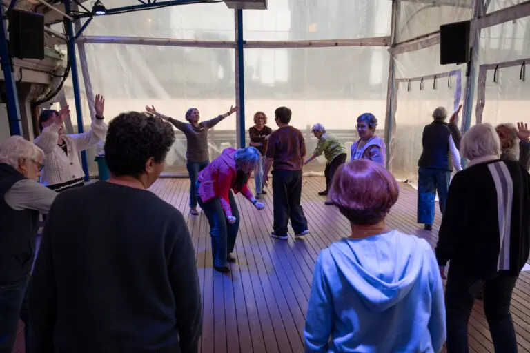 A photograph of a group of seniors in a circle doing movement exercises.