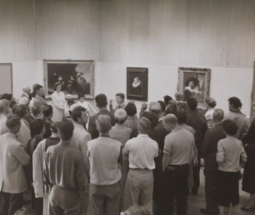 An archival photograph in black and white of large group of people in the Gallery for a tour, led by Doris Shadbolt.