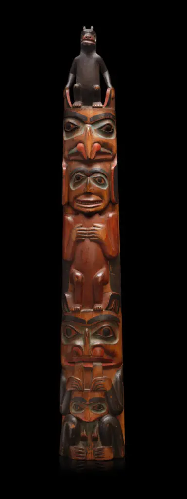 A photograph of a wooden totem pole carving on a black background