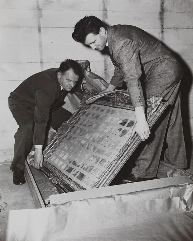 An archival photograph in black and white of two men lifting a painting