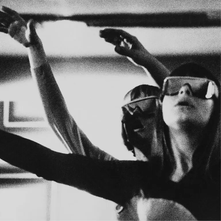 An archival photograph of two people with arms up wearing sunglasses.