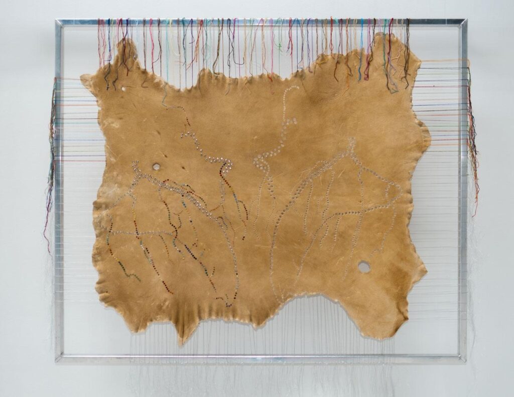 Deer hide stretched on a metal frame by colourful thread.