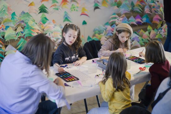 A group of one adult woman and four girls sit at a table painting.