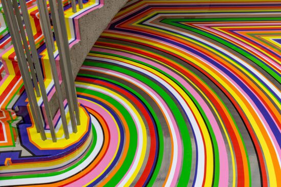 A detailed photograph of Jim Lambie's artwork on the Gallery Rotunda's floor. The shot is looking at a detail of the floor covered in brightly coloured strips of vinyl in purple, pink, green, red, orange and yellow.