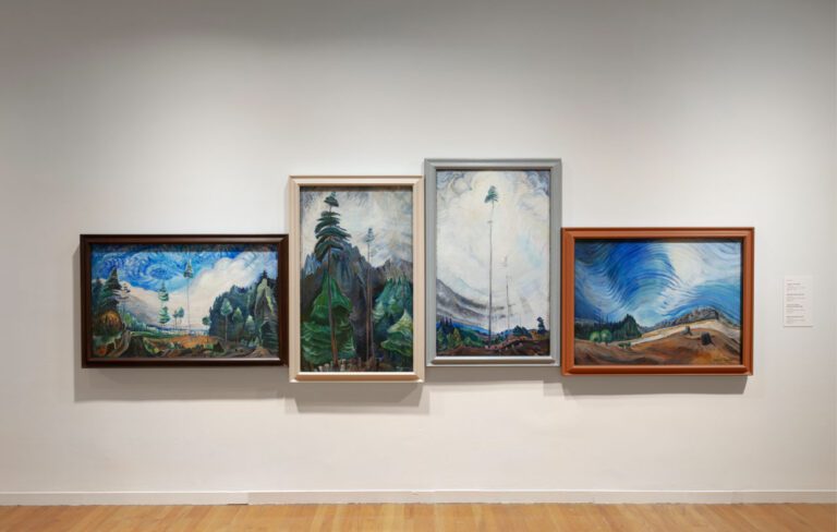 An installation photograph of 4 paintings by Emily Carr hung on the wall so that their horizon lines flow from one to the next.