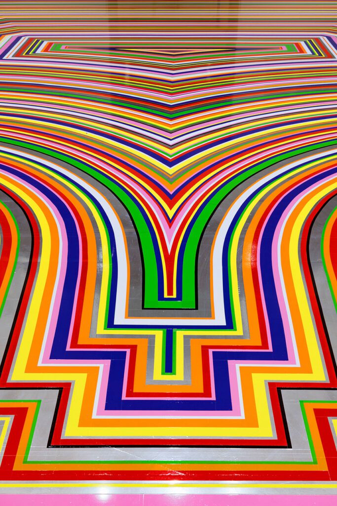 A detail photograph of Jim Lambie's artwork on the Gallery Rotunda's floor. The shot is looking at a detail of the floor covered in brightly coloured strips of vinyl in purple, pink, green, red, orange and yellow.