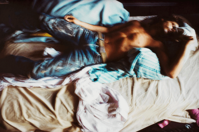 An animated gif of three artworks. The first is a video still by Nan Goldin of a slightly out-of-focus photograph of a shirtless man in denim blue jeans lying on a settee chair covered in wrinkled ivory and pastel blue sheets. The second is a photograph of an Indigenous installation artwork by Beau Dick of a large wooden whale with a small doll-like figurine of the artist on the whale's back. And the third is a detailed photograph of Jim Lambie's artwork on stairs. The shot is looking down a flight of stars that are covered in brightly coloured strips of vinyl in purple, pink, green, red, orange and yellow.