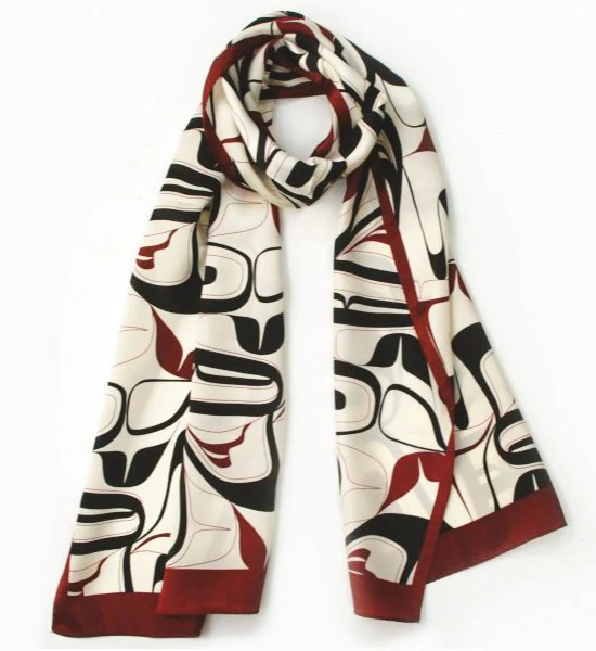 A product photo of a white silk scarf with Indigenous designs on it in black and red