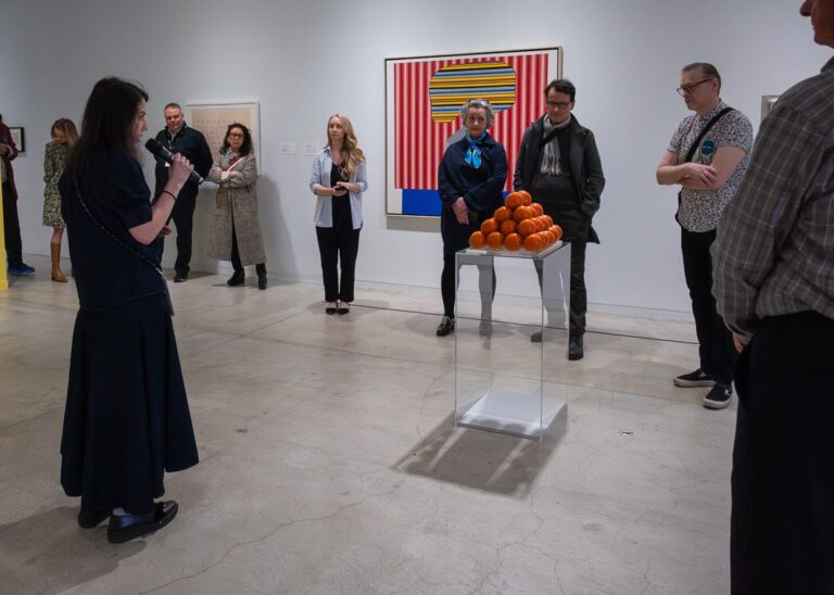 Photograph of a group of people taking a tour at the Gallery, led by a woman in black holding a microphone.