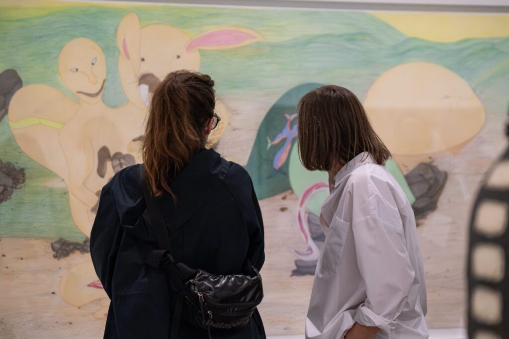 A photograph of two women looking at a large-scale pencil colour drawing by Shuvinai Ashoona.
