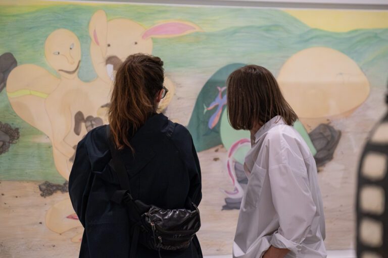 A photograph of two women looking at a large-scale pencil colour drawing by Shuvinai Ashoona.